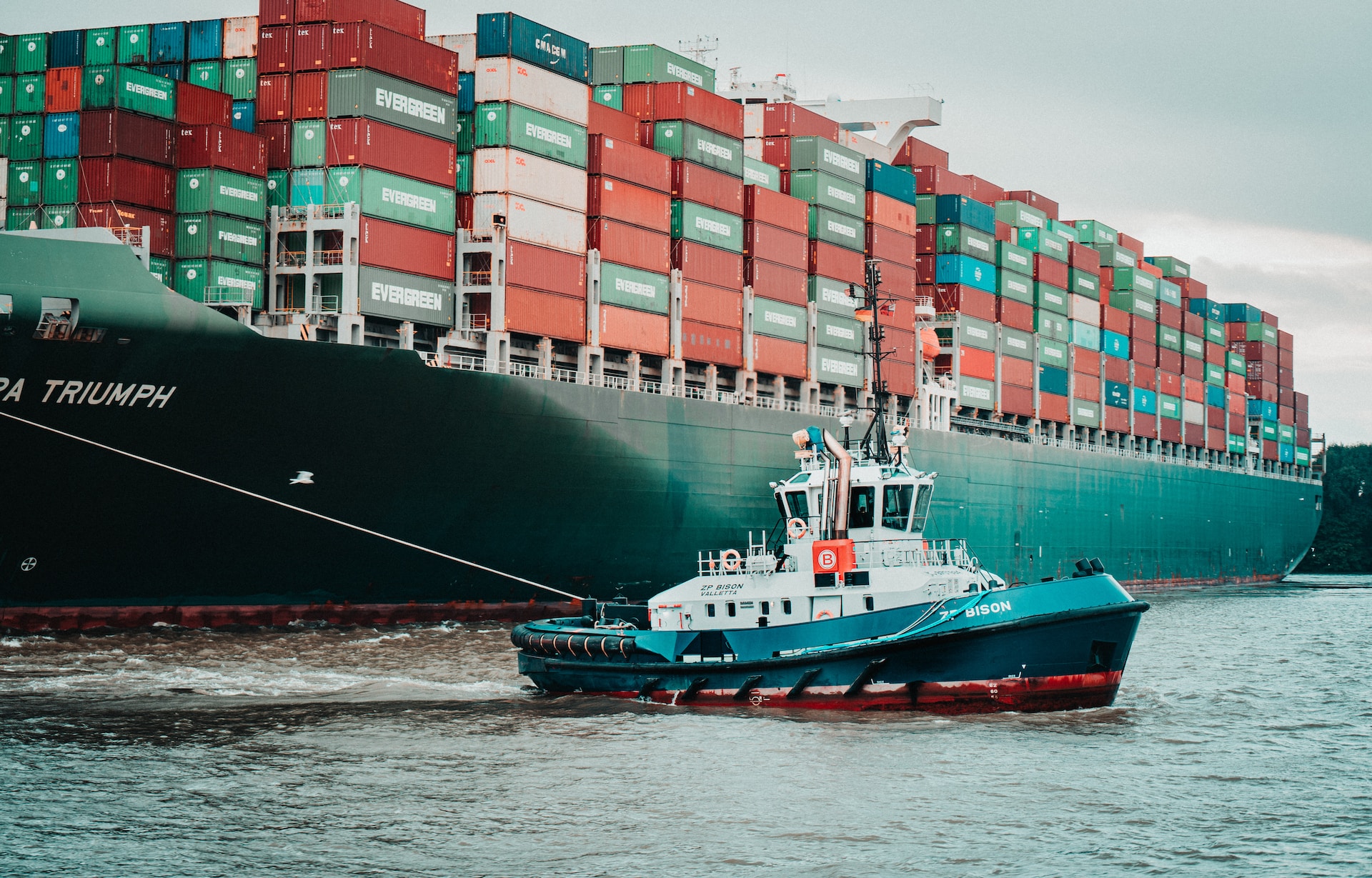 Tug boat pulling a large container ship. Image: Mika Baumeister on Unsplash